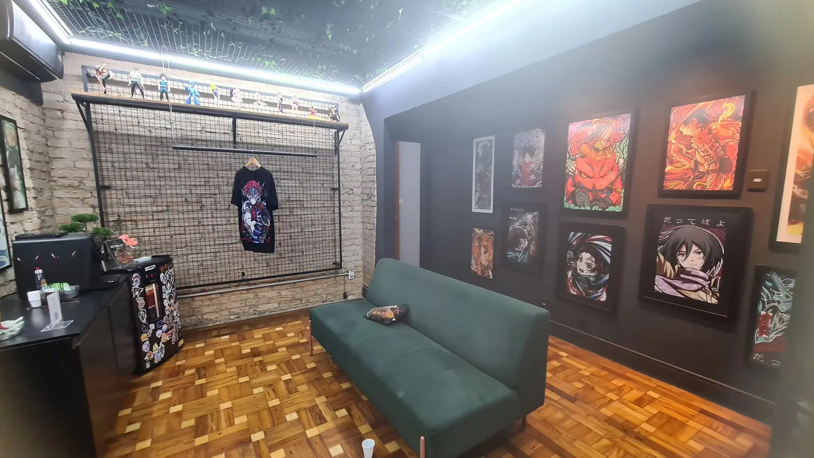 Sala do estúdio com sofá verde e quadros de anime na parede