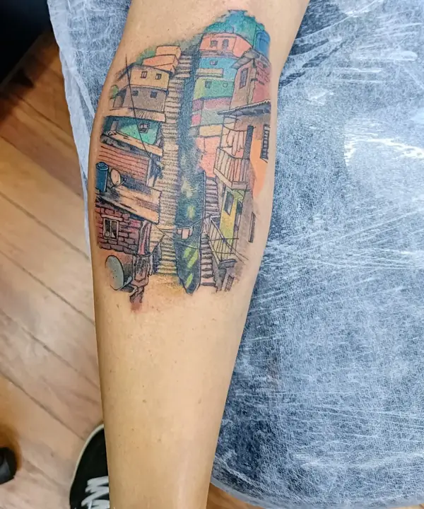 Tatuagem colorida na panturrilha, com casas e uma escadaria